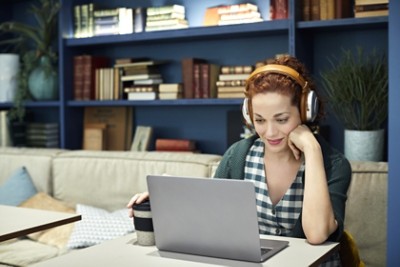 Young businesswoman wearing headphones while using laptop at cafeteria. Female entrepreneur is sitting with disposable coffee cup. Professional is working at creative office.